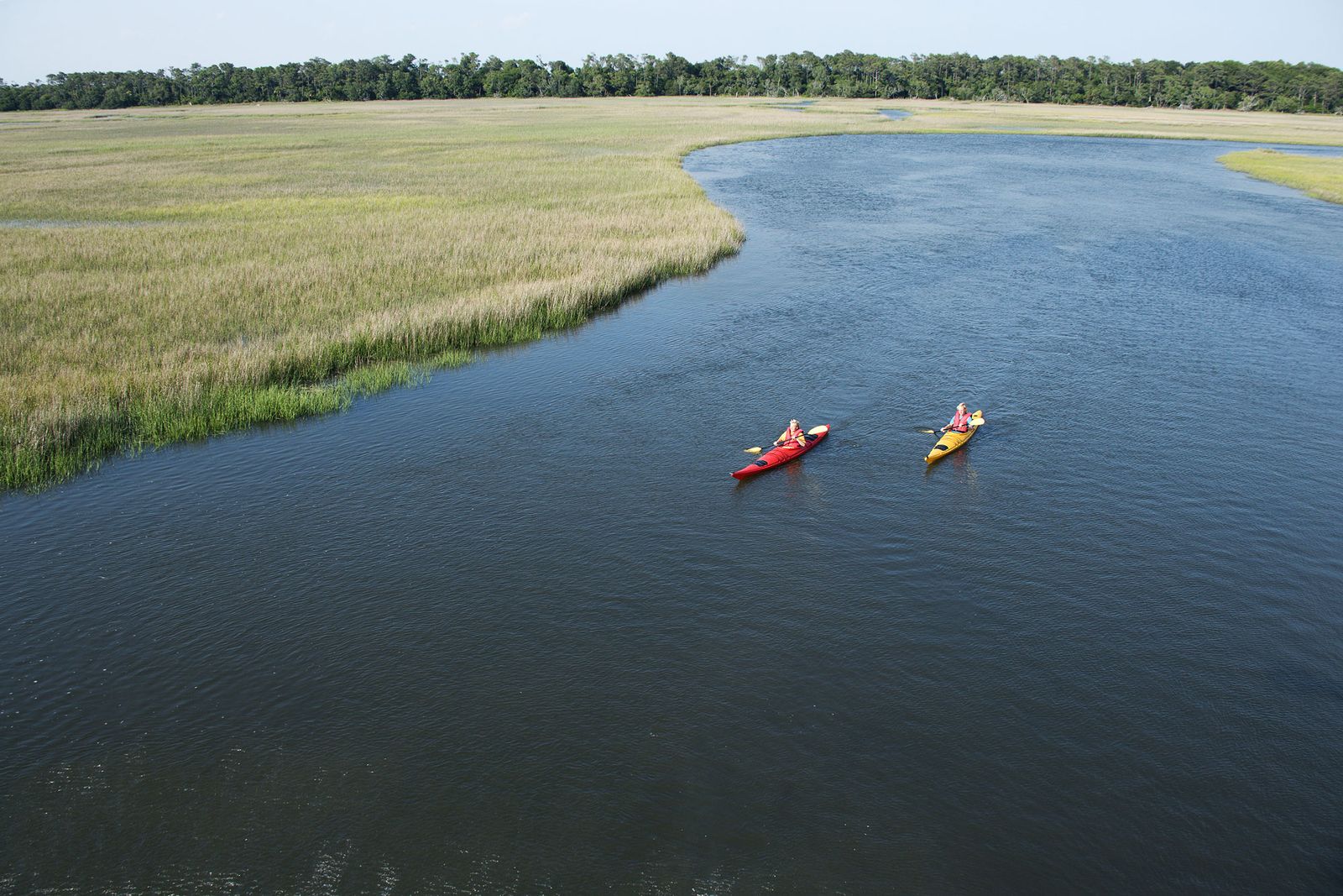 Two kayakers paddling a tidal creek through salt marsh near Bald Head Island